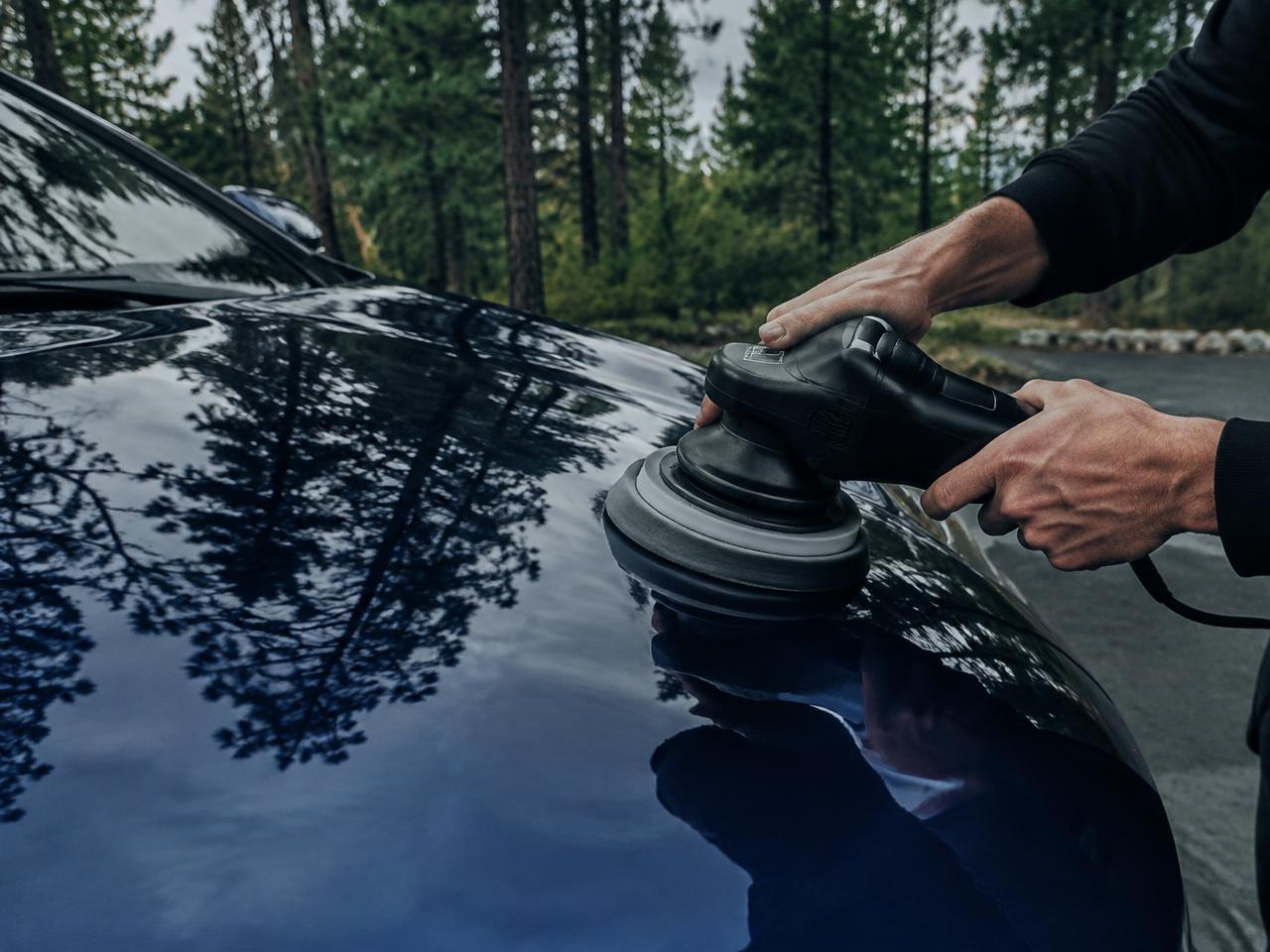 Polisher refining the paint on a dark blue car hood